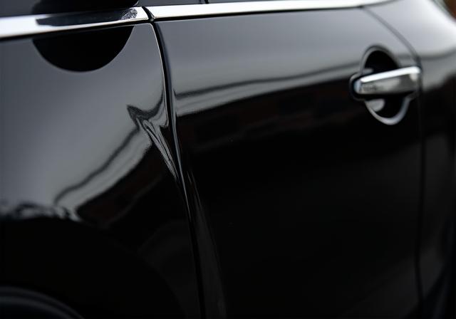 The same black car panel with a perfect, mirror-like finish after paint correction.