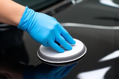 A gloved hand carefully applying ceramic coating to a car's bonnet.